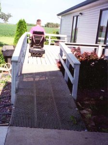 A person driving their wheelchair up a expanded steel ramp to access a home.